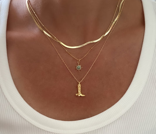 Gold necklaces with a turquoise sun pendant and boot pendant necklace on a mdoel wearing a white top